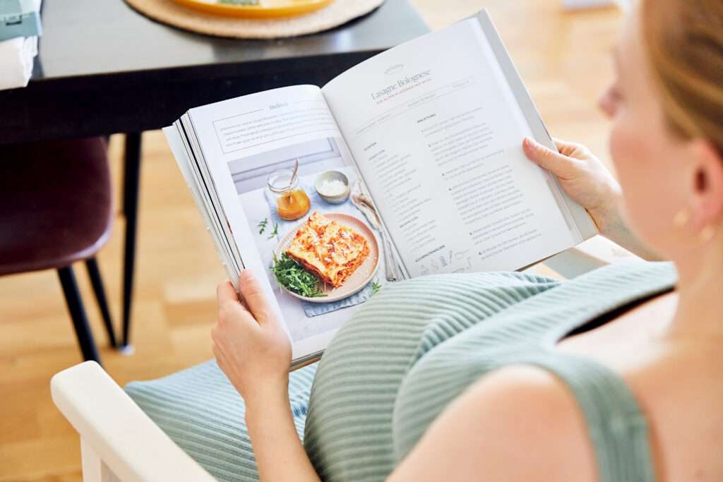 Meal Prepping is lifesaver for Postpartum, pregnant woman reading cookbook for newborn parents